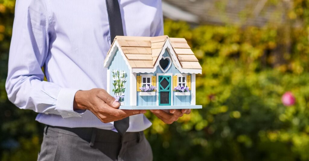 A man holds a small model house, illustating an inherited property